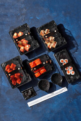 Various rolls packed in plastic containers with ginger, soy sauce, chopsticks on table