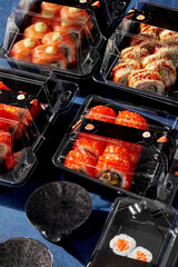 Set of sushi rolls packed in plastic takeaway containers with ginger and soy sauce