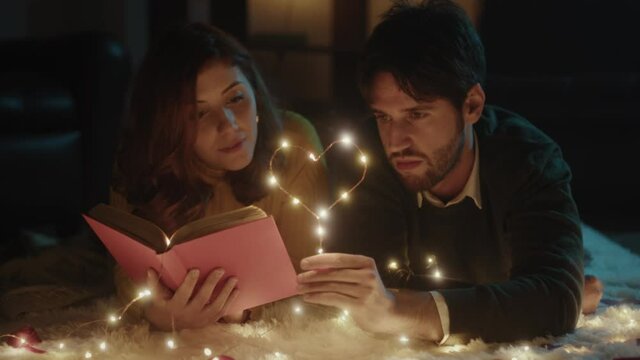 Ragazzo e ragazza su tappeto bianco per San Valentino con cuore in filo di luci led legge libro