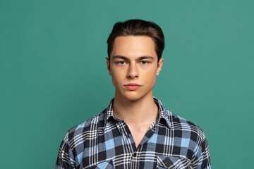 Close-up young handsome calm man, student wearing warm plaid shirt isolated on green studio background.