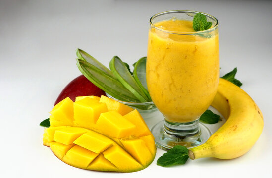 Mango, banana, aloe vera slices, aloe leaf, mint sprigs, yellow smoothies. Close up