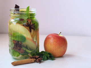 Mug of detox water with red apple slices, mint leaves, anise stars, cinnamon stick. Accompanied with an apple, mint branches, pieces of star anise and cinnamon