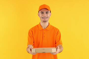 Attractive delivery man with pizza box on yellow background