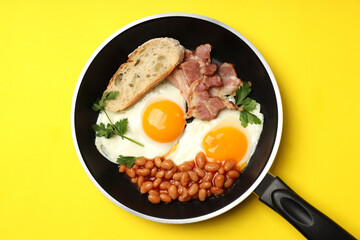 Pan with tasty breakfast on yellow background