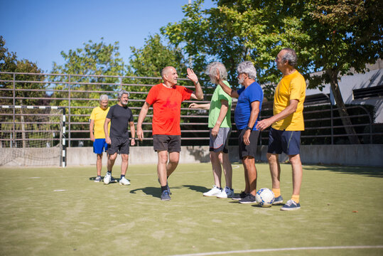 Senior men thanking each other after match. Men with grey hair in sport clothes standing in row on sport field, giving high fives. Football, sport, leisure concept - Powered by Adobe