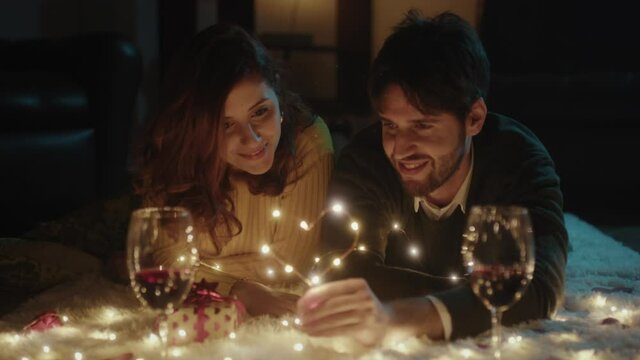 Ragazzo e ragazza su tappeto bianco per San Valentino con cuore in filo di luci led legge libro