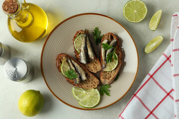 Concept of tasty snack with sandwiches with sprats on light textured background