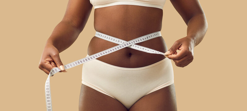 Narrow banner crop shot of African American woman with curves measure waist with tape. Ethnic girl insecure about natural body shape unhappy with fat obesity. Diet and wellbeing concept.