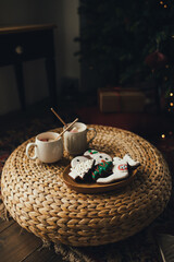 Cocoa with marshmallow, paper straw and gingerbread on wicker table with Christmas tree on the background. Holiday festive decorations.
