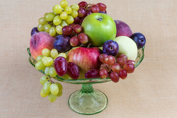 Different fruits in vintage glass fruit vase on cloth surface