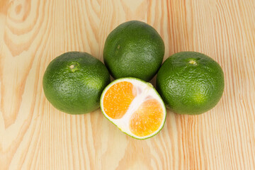 Whole and half of ripe green tangerines on wooden surface