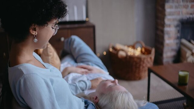 Young girl laying on a lap of her girlfriend sitting on the couch, both laughing. Lesbian couple hugging. Young couple. High quality 4k footage