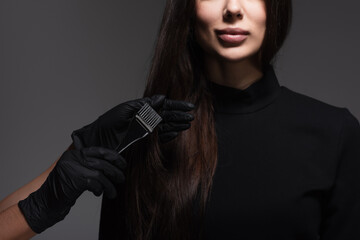 cropped view of hairstylist holding brush near woman with brown hair isolated on dark grey - obrazy, fototapety, plakaty
