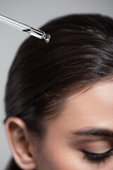 close up of young woman holding pipette with oil near shiny hair isolated on grey