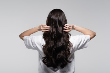 back view of brunette woman adjusting long shiny hair isolated on grey