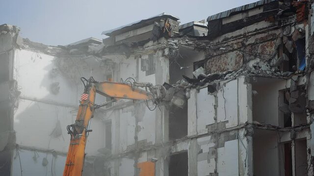 A scoop of demolishing machine breaks off the floors of the destroyed house. Excavator working in the cloud of dust .