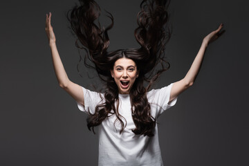 young and amazed woman with wavy hair gesturing on dark grey