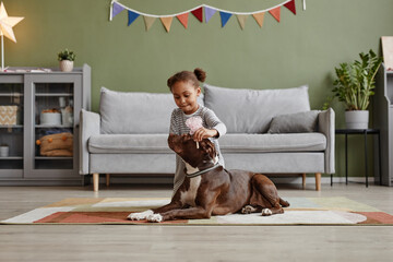 Full length portrait of cute African-American girl playing with big dog at home, copy space