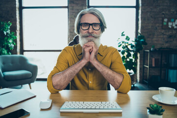 Photo of thoughtful mature guy dressed yellow shirt spectacles looking modern gadget indoors...