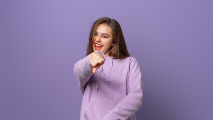 Congrats its you. Cheerful and excited young woman pointing finger at camera and smiling, congratulating you, praising or inviting, standing happy on purple background