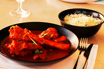 indian lamb or mutton shank curry, also known as nalli rogan josh on dining table with jeera rice