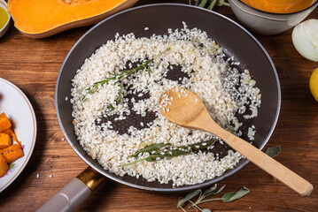 Preparing risotto with pumpkin - raw rice fried in a pan with sage and ingredients for cooking...