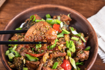 Fried chicken with vegetables in a plate and chopsticks with a piece of chicken close-up - asian cuisine