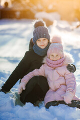 Two cute girls, the youngest and the oldest, are sitting in a winter park and playing with snow. Family values. Winter fun