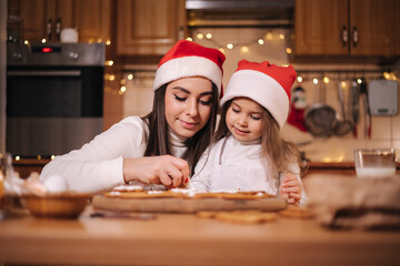 Mom in santas hat with her little doughter decorates gingerbread using glaze. Christmas and New Year traditions concept. Christmas bakery. Happy holidays