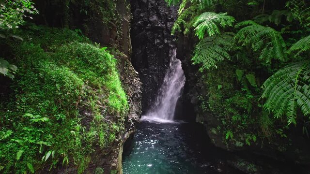 Aerial close up of beautiful waterfall in jungle. Drone flying through the tropical cascade cave. Nature of French Polynesia in Tahiti island.