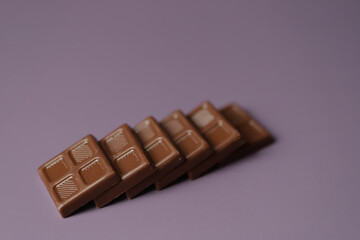 Small square milk chocolate lays on each other in a row.