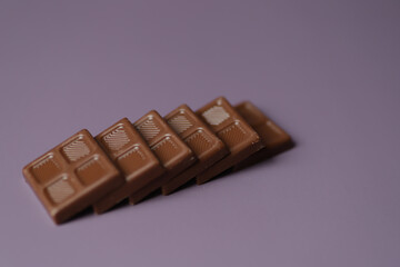 Small square milk chocolate lays on each other in a row.