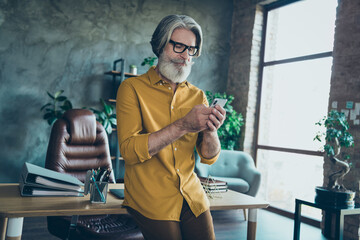 Portrait of attractive focused skilled gray-haired man leader partner using device web search at work place station indoors