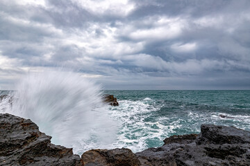 Fototapeta na wymiar Stunning wave splash at rocky shore and scenic clouds
