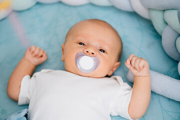 a baby with a pacifier in his mouth lies on a blue diaper. 