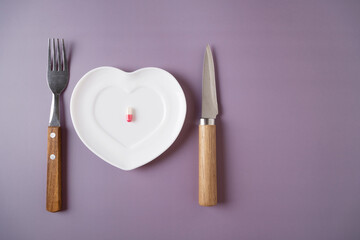 The capsule with the medicine lies on a saucer with a knife and fork