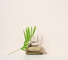 stack of round stones and and green palm leaf on a beige background. Scene for demonstration of cosmetic product