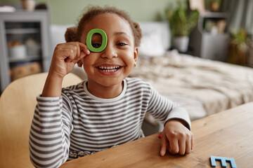 Portrait of cute African-American girl playing with letters and smiling at camera, copy space