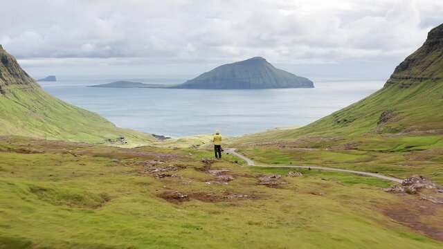 Aerial view of unrecognizable man looking at the panorama, islands, ocean, green mountain and rock cliffs.Impressions of the fascinating archipelago of the Faroe Islands in the North Atlantic Ocean