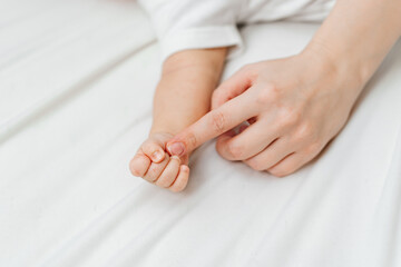 a small baby's hand and a mother's hand on a white sheet. 