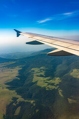 Naklejka premium View of airplane wing, blue skies and green land during landing. Airplane window view.