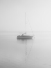 Sailboat on flat calm water with furled sails in eerie quiet morning fog