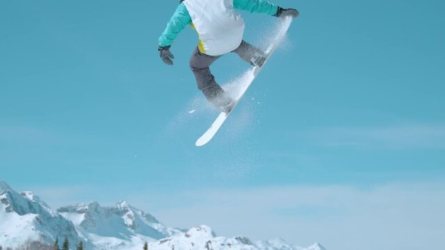 SLOW MOTION Snowboarder flies through the air and does a spinning nose grab while having fun in a snowpark in sunny Julian Alps. Awesome shot of a man doing stunts while riding in Vogel snowboard park