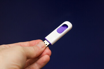 flash drive made of white plastic with purple inserts on a blue background in hand