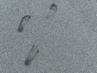 Fototapeta na wymiar Traces of human feet on the sea sand. Background texture: summer beach walks. Footprint on the sandy seashore.