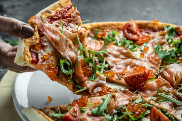 Woman hand hold Sliced pizza with salmon, red caviar, tomatoes and aragula. Traditional italian cuisine. Delicious breakfast or snack