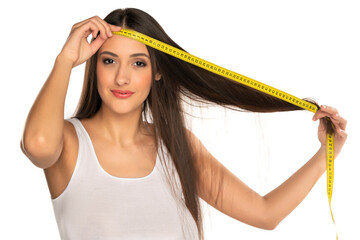a young happy woman shows the length of her hair with a measuring tape