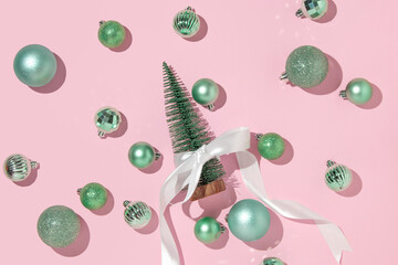 Creative layout with Christmas tree with white satin ribbon bow and green baubles on pastel pink...
