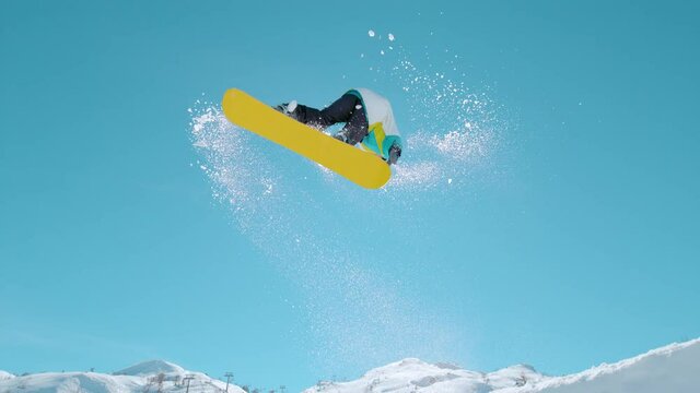 SLOW MOTION, BOTTOM UP, LENS FLARE: Athletic male tourist snowboarding in the sunny Julian Alps does a spinning trick as he takes off a massive kicker. Action shot of a pro doing snowboarding stunts.
