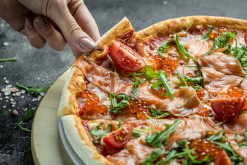 Female hands holding delicious pizza with salmon, red caviar, tomatoes and aragula. italian pizza